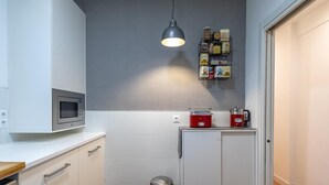 A compact kitchen with white cabinets, a microwave, a red coffee maker, and a trash bin.