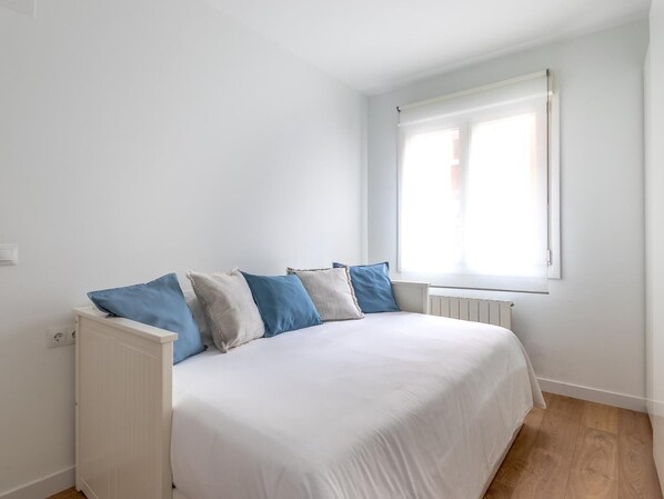 A bedroom with a bed, white walls, a window, and a radiator.