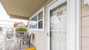 Un immeuble résidentiel avec une porte numérotée (206), un porche couvert avec des chaises et un petit jardin.