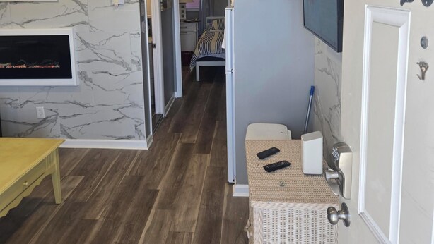 Une chambre d’hôtel avec un mur décoré d’un motif imitant le marbre, une télévision, un fauteuil en osier et une porte portant le numéro 20.