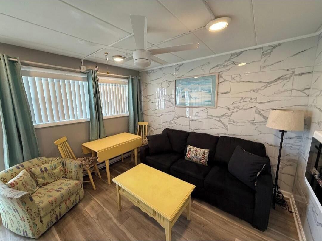 Un salon comprenant un canapé, une petite table, un fauteuil, un ventilateur de plafond et une cheminée.