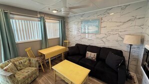 Un salon comprenant un canapé, une petite table, un fauteuil, un ventilateur de plafond et une cheminée.