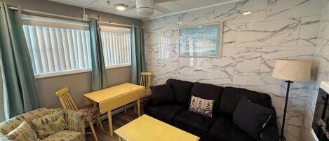 Un salon comprenant un canapé, une petite table, un fauteuil, un ventilateur de plafond et une cheminée.