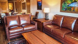 A living room with leather sofas, a wooden coffee table, and a painting of a landscape. - Cabin, Prem unit w/ bal & jet tub. Sleeps 4. Avail. Wed 12/23/26 to Sun 12/27/26 (Gatlinburg)