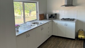 Une cuisine moderne avec des meubles blancs, un évier en acier inoxydable, une cuisinière à gaz et une fenêtre donnant sur un jardin.
