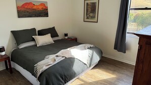 Une chambre avec un grand lit, une table de chevet, une fenêtre donnant sur l’extérieur et deux tableaux encadrés accrochés au mur.