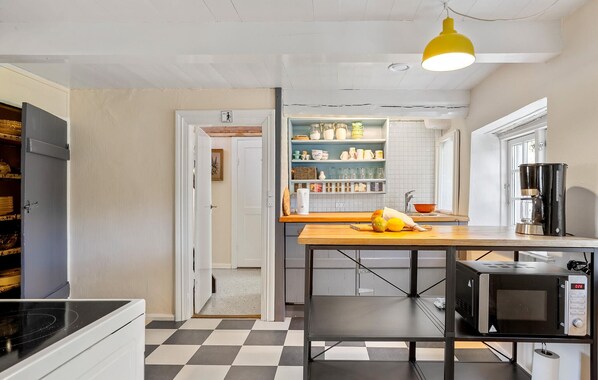 A kitchen with a checkered floor, a microwave, a coffee maker, and a shelf with various kitchen items.