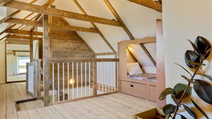 Un dormitorio tipo loft con vigas de madera a la vista, una escalera de madera, una cama con cabecero blanco y una planta en maceta.