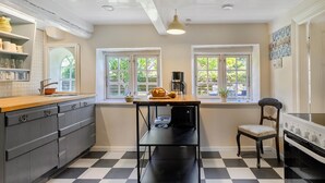 Una cocina con piso a cuadros, una cafetera, una hogaza de pan y una silla.