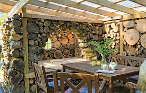 A wooden outdoor dining area with a table and chairs, surrounded by a wall of stacked logs.