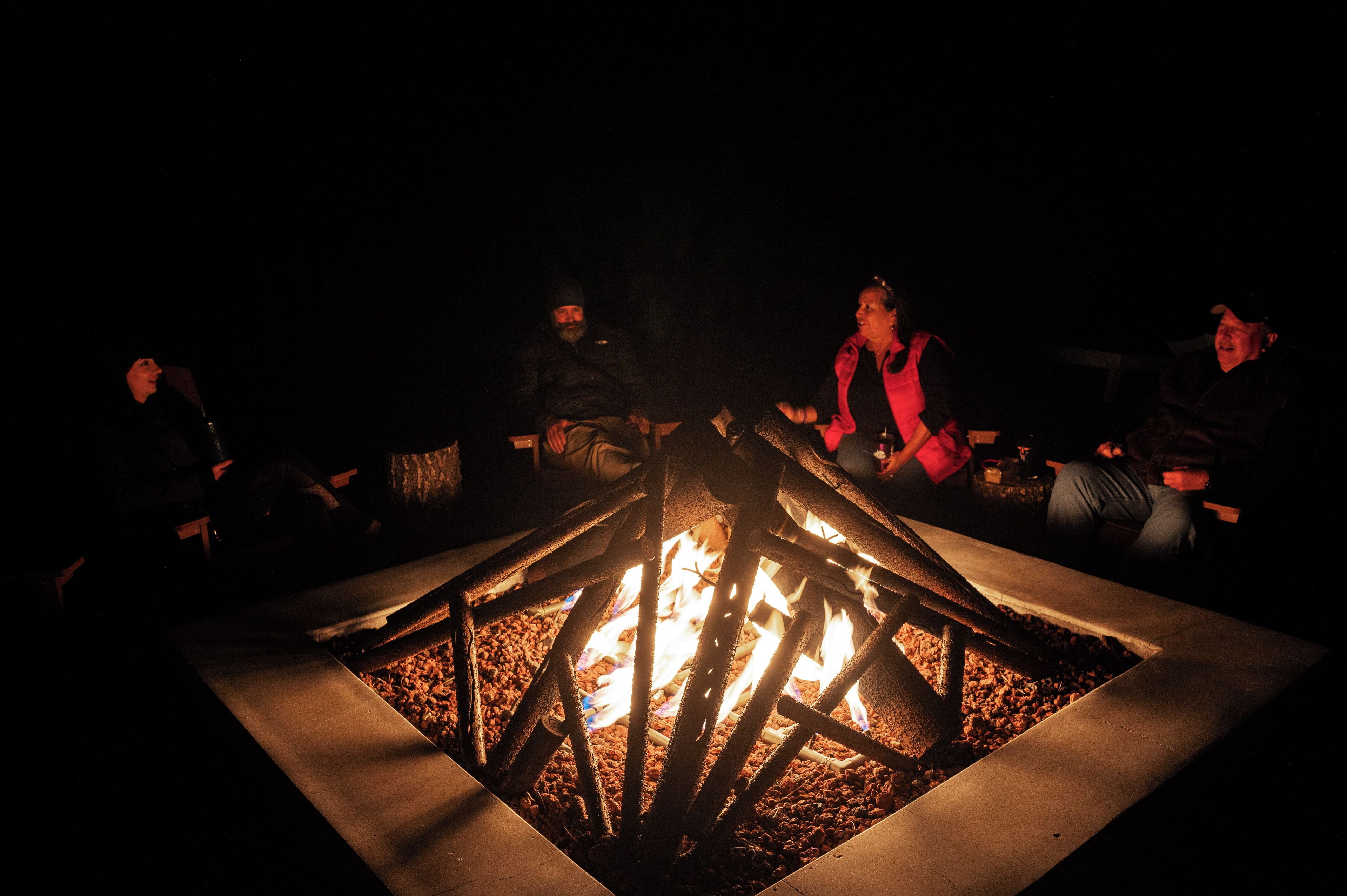 A group of people seated around a fire pit at night.