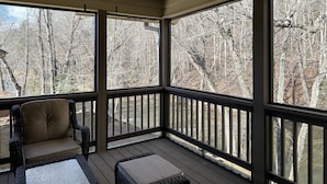 Eine überdachte Veranda mit Deckenventilator, großen Fenstern und Korbmöbeln.