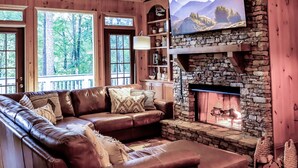 A cozy cabin interior with a stone fireplace, leather sofa, wooden ceiling, and large windows. - Discover family fun and serenity at Big Canoe resort! (Jasper, GA)