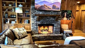 A cozy living room with a stone fireplace, leather sofa, and a bookshelf filled with books and decorative items. - Discover family fun and serenity at Big Canoe resort! (Jasper, GA)