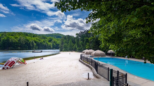 A beach with a swimming pool, umbrellas, and a lifeguard stand. - Discover family fun and serenity at Big Canoe resort! (Jasper, GA)