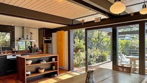 Eine moderne Küche mit Holzböden, ein Essbereich mit großem Tisch und Blick auf einen Garten durch große Schiebetüren.