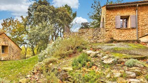 Ein Steinhaus mit rustikalem Aussehen, umgeben von einem Garten mit verschiedenen Pflanzen und einer Steinmauer.