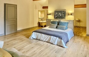 A bedroom with a wooden floor, a bed with a grey and white duvet, two bedside lamps, a wall-mounted mirror, and a classic clawfoot bathtub. - Mas De La Petite Folie (Entrechaux)