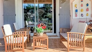 A patio with wooden chairs and a table, a potted plant, and a view of a garden through glass doors. - Gorgeous home in Graveson with WiFi (Graveson)
