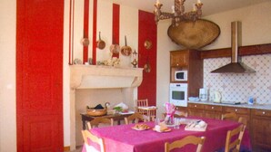 A dining area with a red tablecloth, wooden chairs, and a kitchen in the background.