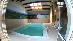An indoor swimming pool with a mural on the wall, a ceiling with wooden beams, and white lounge chairs.