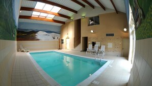 An indoor swimming pool with a tiled floor, a mural on the wall, and a staircase leading to an upper level.