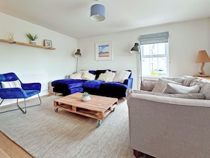 A living room with a sectional sofa, a blue armchair, a wooden coffee table, and a grey sofa. - A newly built haven located near Westward Ho. (Appledore)