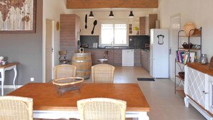 A compact kitchen with wooden cabinets, a white refrigerator, and a dining area with wicker chairs and a wooden table.