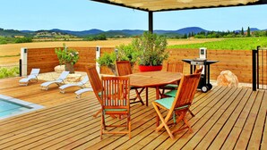 A wooden deck with a table and chairs, a barbecue grill, and a pool.