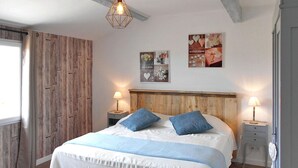 A bedroom with a wooden headboard, a large bed with blue and white bedding, two bedside lamps, and a wall with framed pictures.