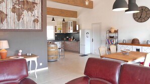 A spacious living area with a large world map on the wall, wooden beams, a dining table with chairs, and a kitchen in the background.