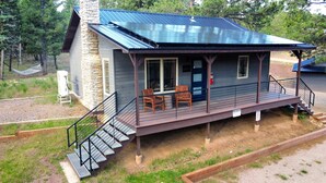 A cabin with a stone chimney, a porch with chairs, and a metal roof. - Spectacular Cabin in the Woods, Fire Pit, King Bed, Remodled, A/c (Angel Fire)
