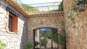 A stone-walled courtyard with a tiled floor, a glass door entrance, and potted plants.