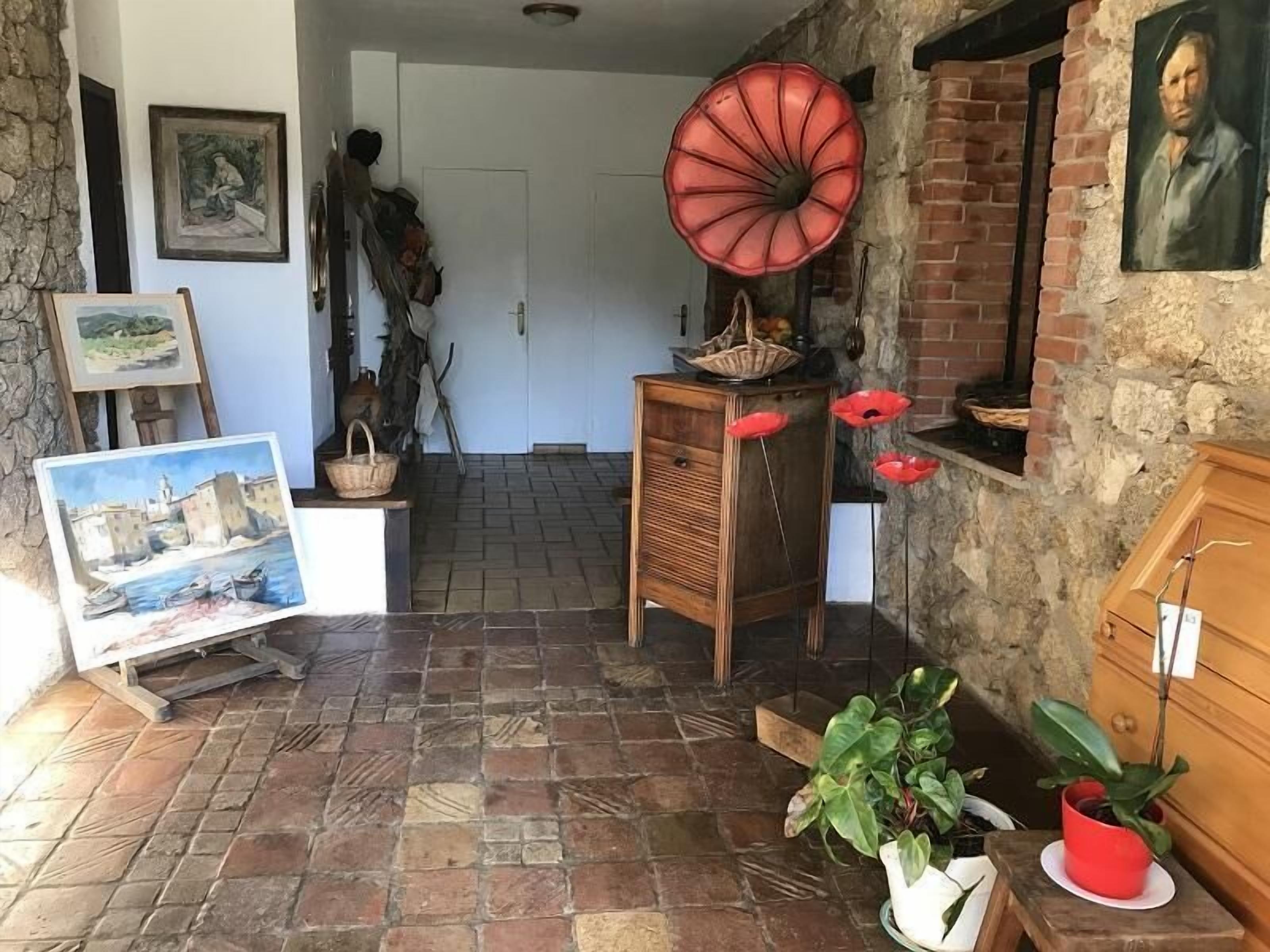 Een landelijk interieur met een betegelde vloer, een houten kast, een rode decoratie en een schilderij aan de muur.