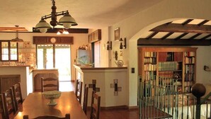 A dining area with a wooden table and chairs, a chandelier, and a staircase leading to a library with bookshelves.