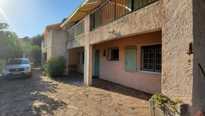 Un patio empedrado con un vehículo estacionado, un edificio con balcón y un pequeño jardín.