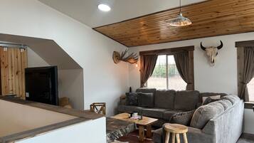 Een gezellige woonkamer met een houten plafond, een bank, een salontafel en een rustieke inrichting, waaronder een hertenkop en een kooiskedel.