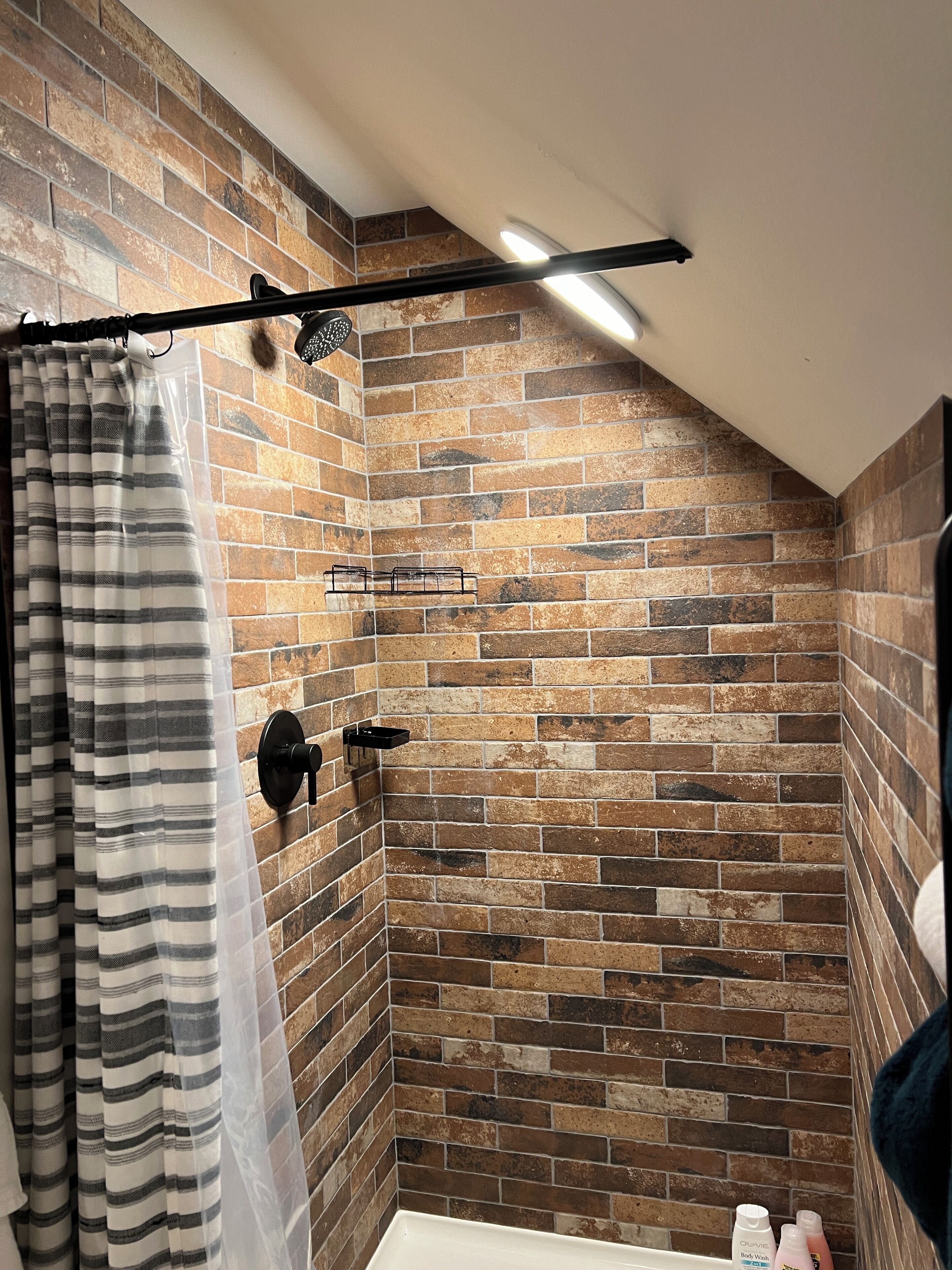 Une salle de bain avec un mur en briques, un rideau de douche, un porte-serviettes et une petite étagère contenant des articles de toilette.