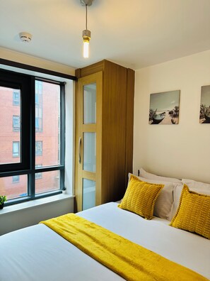 A bedroom with a bed, a window, a wooden wardrobe, and two wall-mounted pictures.