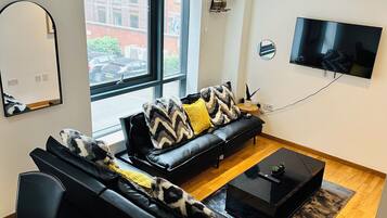 A modern living room with a black leather sofa, a coffee table, and a flat-screen TV mounted on the wall.