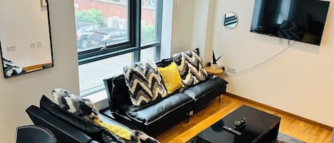 A modern living room with a black leather sofa, a coffee table, and a flat-screen TV mounted on the wall.