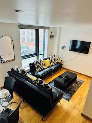 A modern living room with a black leather sofa, a coffee table, and a flat-screen TV mounted on the wall. - Luxury 2 Bedroom Apartment in City Centre  (Liverpool)
