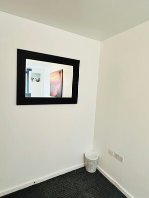 A room with a framed artwork on the wall, a white trash bin, and electrical outlets on the wall. - Luxury 2 Bedroom Apartment in City Centre  (Liverpool)