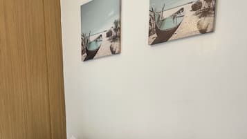 A bed with white bedding and two yellow pillows, a wooden door, and two wall-mounted pictures of boats on a beach.