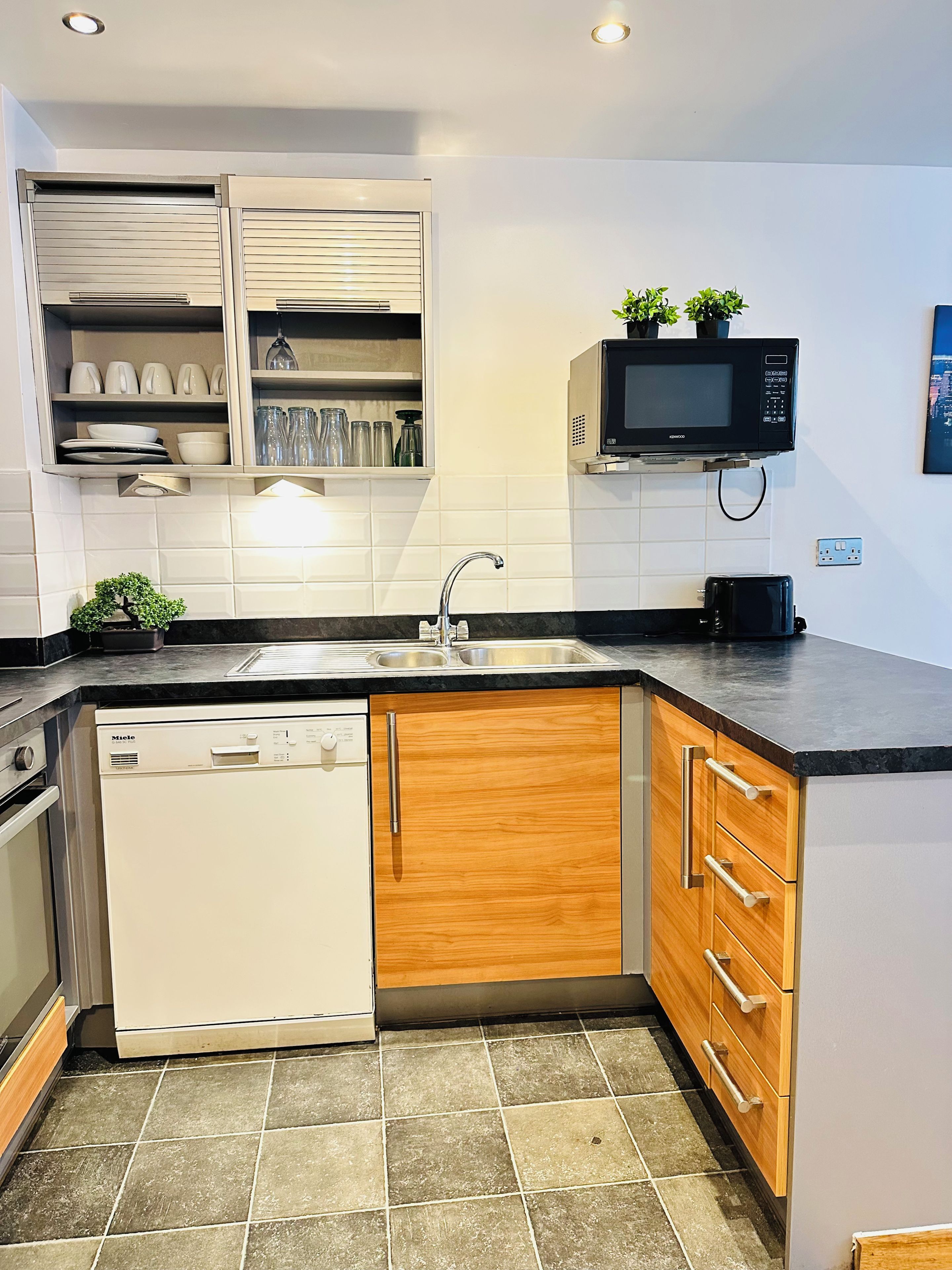 A compact kitchen with a dishwasher, wooden cabinets, a microwave, and a sink.