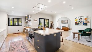 Cozinha moderna com ilha central, área de jantar com sofá verde e sala de estar com uma pintura grande.