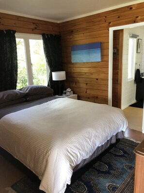 Una camera da letto con un letto grande, pareti in legno, un comodino con una lampada, un quadro e vista sull'esterno.