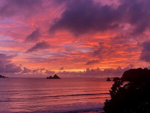 Tramonto su un mare calmo, con affioramenti rocciosi.