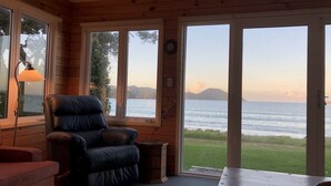 Ein gemütliches Cabin-Zimmer mit Ledersessel, kleinem Tisch und großen Fenstern mit Blick auf Wasser und Hügel.
