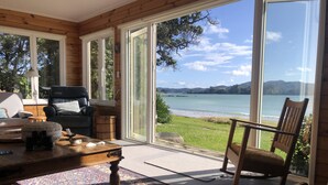 Ein Zimmer mit einer großen Schiebetür und einem herrlichen Blick auf einen See und Berge. Im Raum befindet sich ein Holztisch, ein Teppich mit Muster, ein schwarzer Ledersessel und eine Couch.